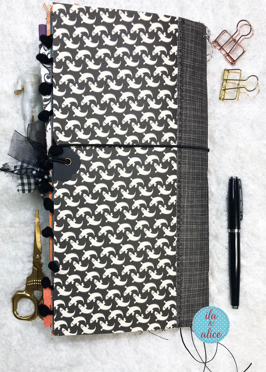 Handmade Halloween junk journal with black and white pattern of ghosts a textured surface with stationery items.