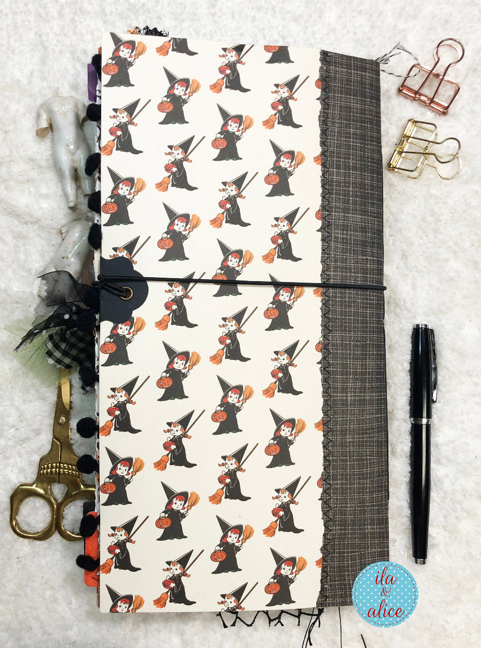 Handmade Halloween junk journal with witch pattern on a textured surface with stationery items.