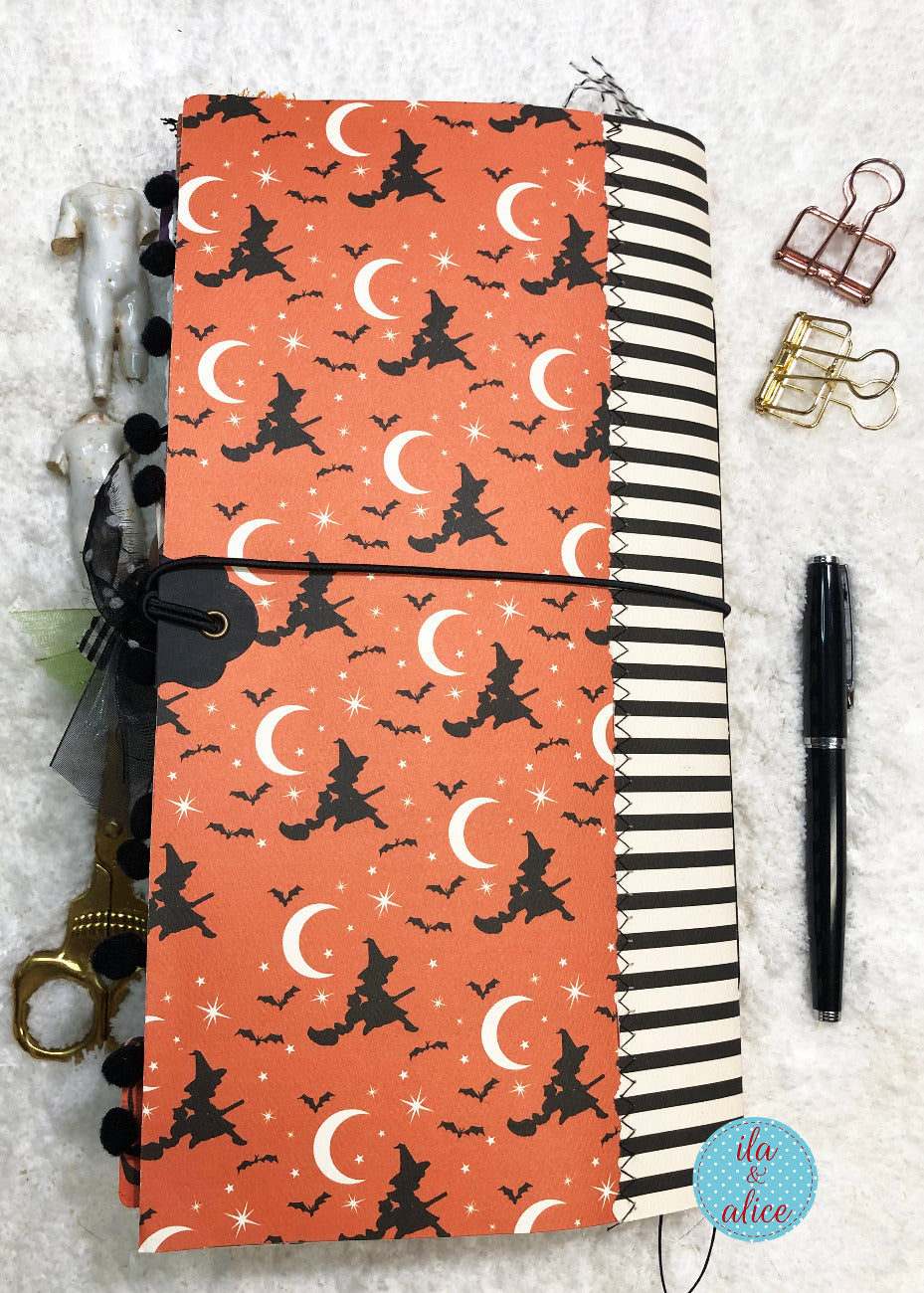 Handmade Halloween junk journal with Halloween-themed cover featuring witches and moons on a textured surface.