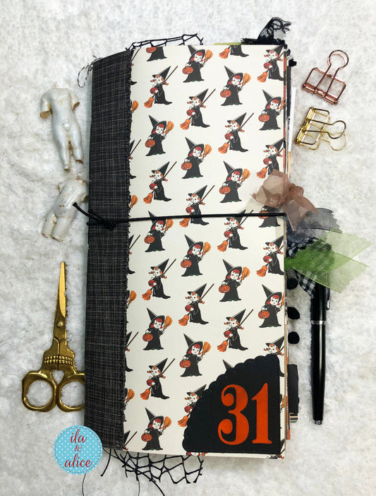 Junk Journal with Halloween-themed cover featuring tiny witches in witch hats and brooms, surrounded by decorative items on a textured surface.