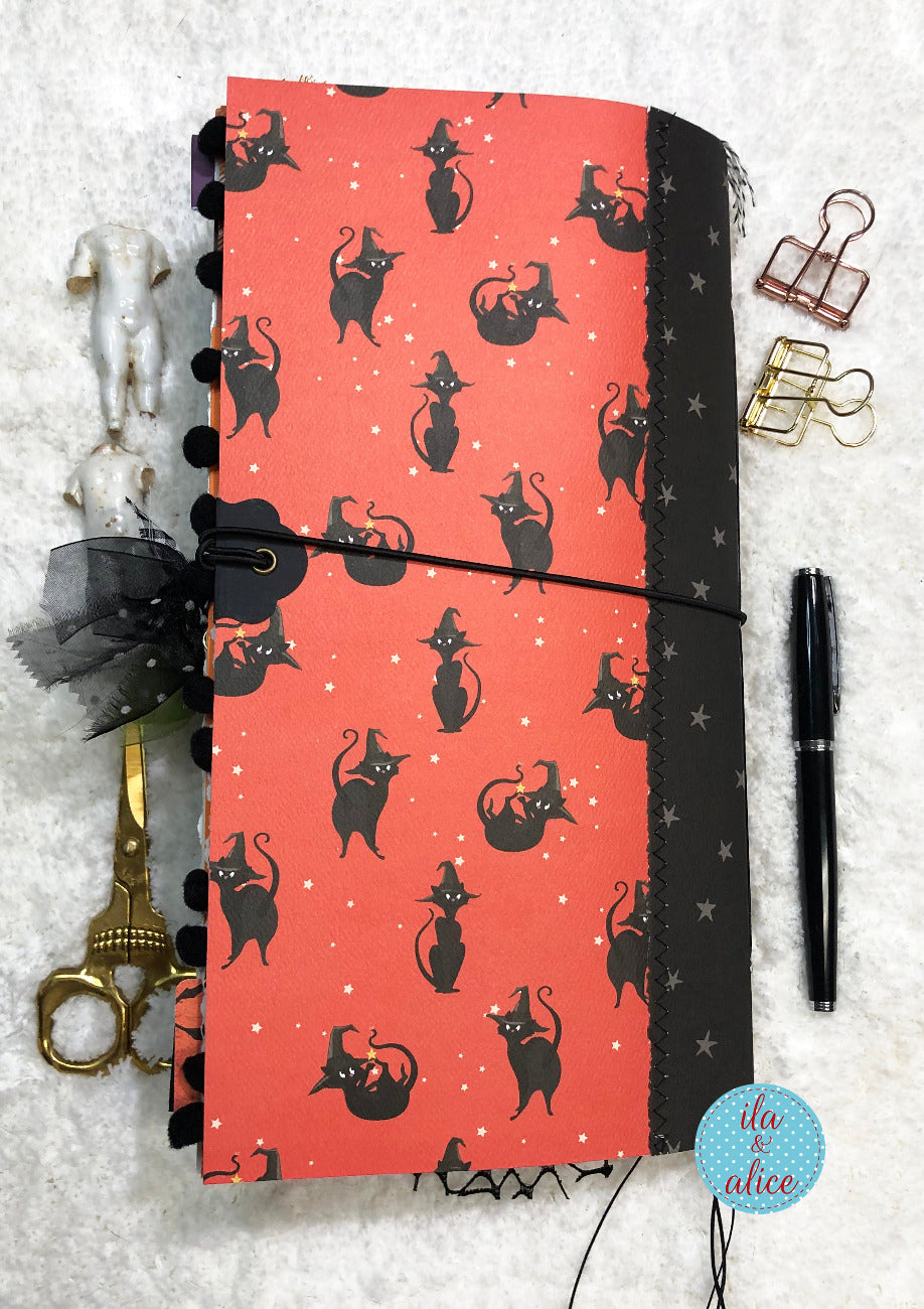 Handmade made Halloween junk journal with black cat pattern and number 31 on an orange background surrounded by stationery items on a textured surface.