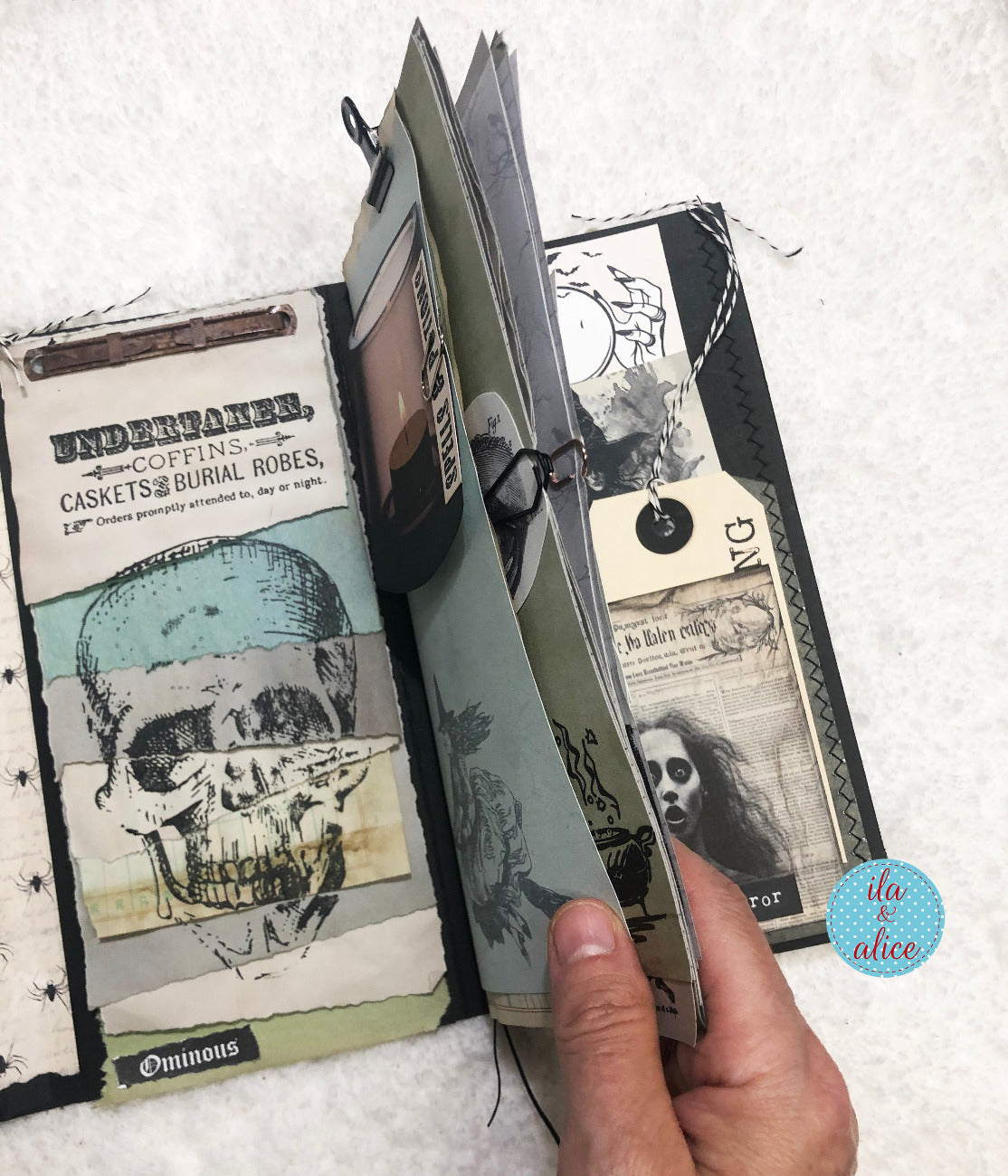 Hand holding a handmade Halloween folio with skull illustrations on a textured white background