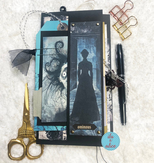 Handmade Halloween folio with female ghost figure, scissors, pen, and decorative elements on a textured surface.