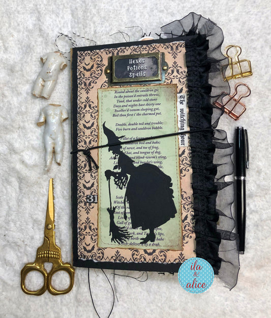 Handmade Halloween junk journal with a witch silhouette and text, surrounded by scissors, paper clips, and a pen on a textured surface.