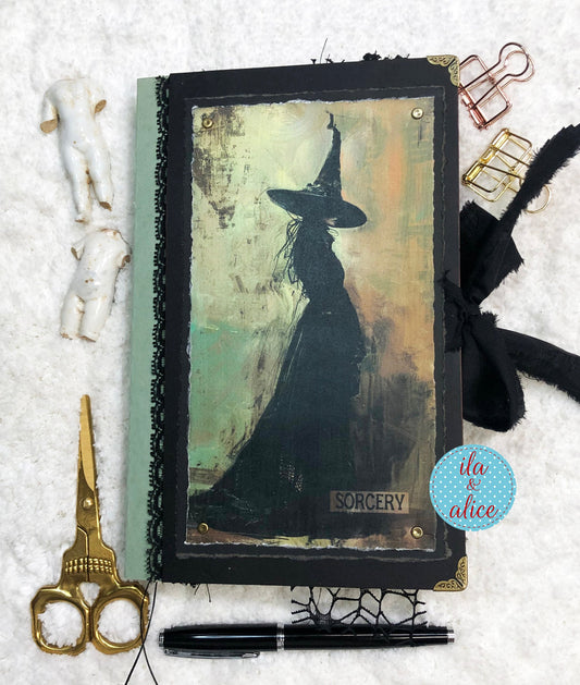 Journal with witch illustration and 'Sorcery' text, surrounded by decorative items on a textured surface.