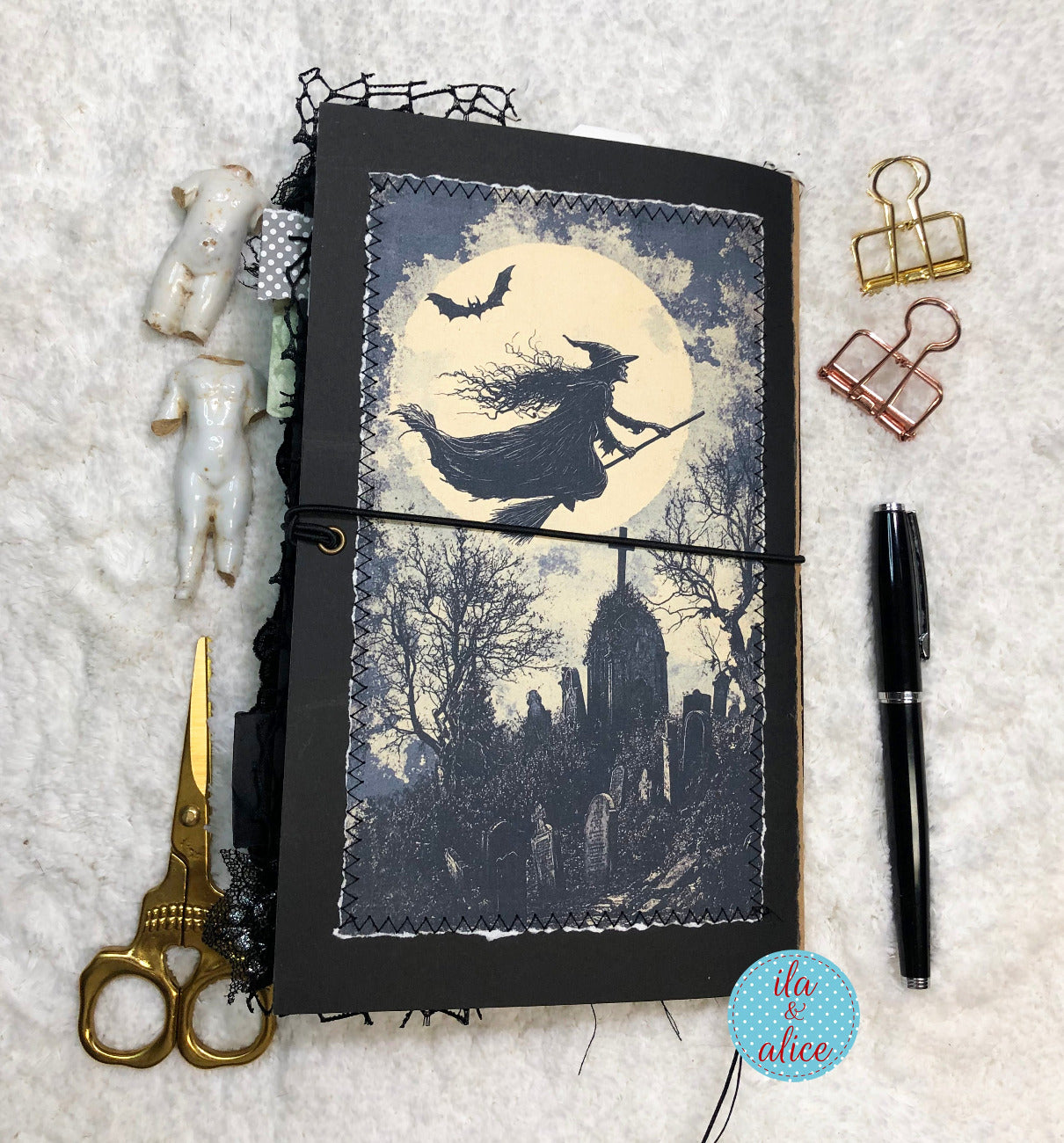 Decorative notebook with Halloween-themed cover featuring a witch on a broomstick, surrounded by decorative items like scissors and pins.