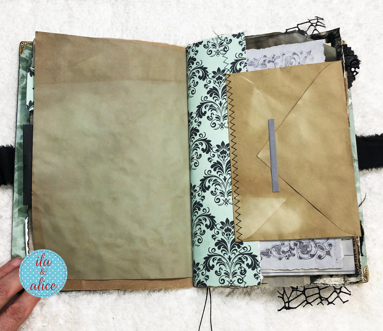 Handmade Eerie Halloween Gothic junk journal with decorative pages and a brown envelope on a textured surface.