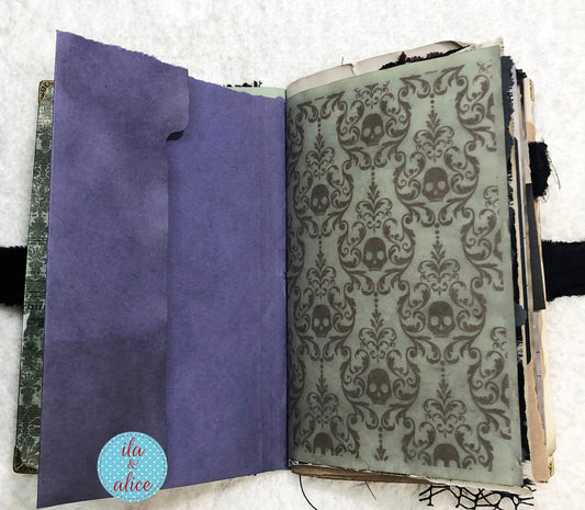 Handmade Eerie Halloween Gothic junk journal with purple interior page and skull patterned cover on a textured surface.