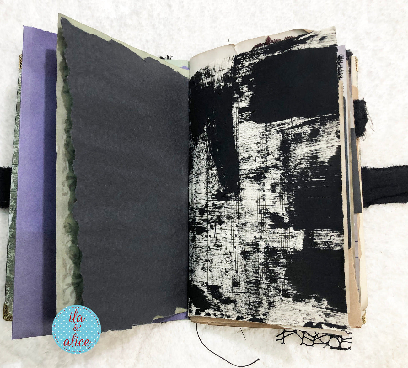 Handmade Eerie Halloween Gothic junk journal with textured black and white pages on a textured surface, featuring the brand 'ila & alice'.