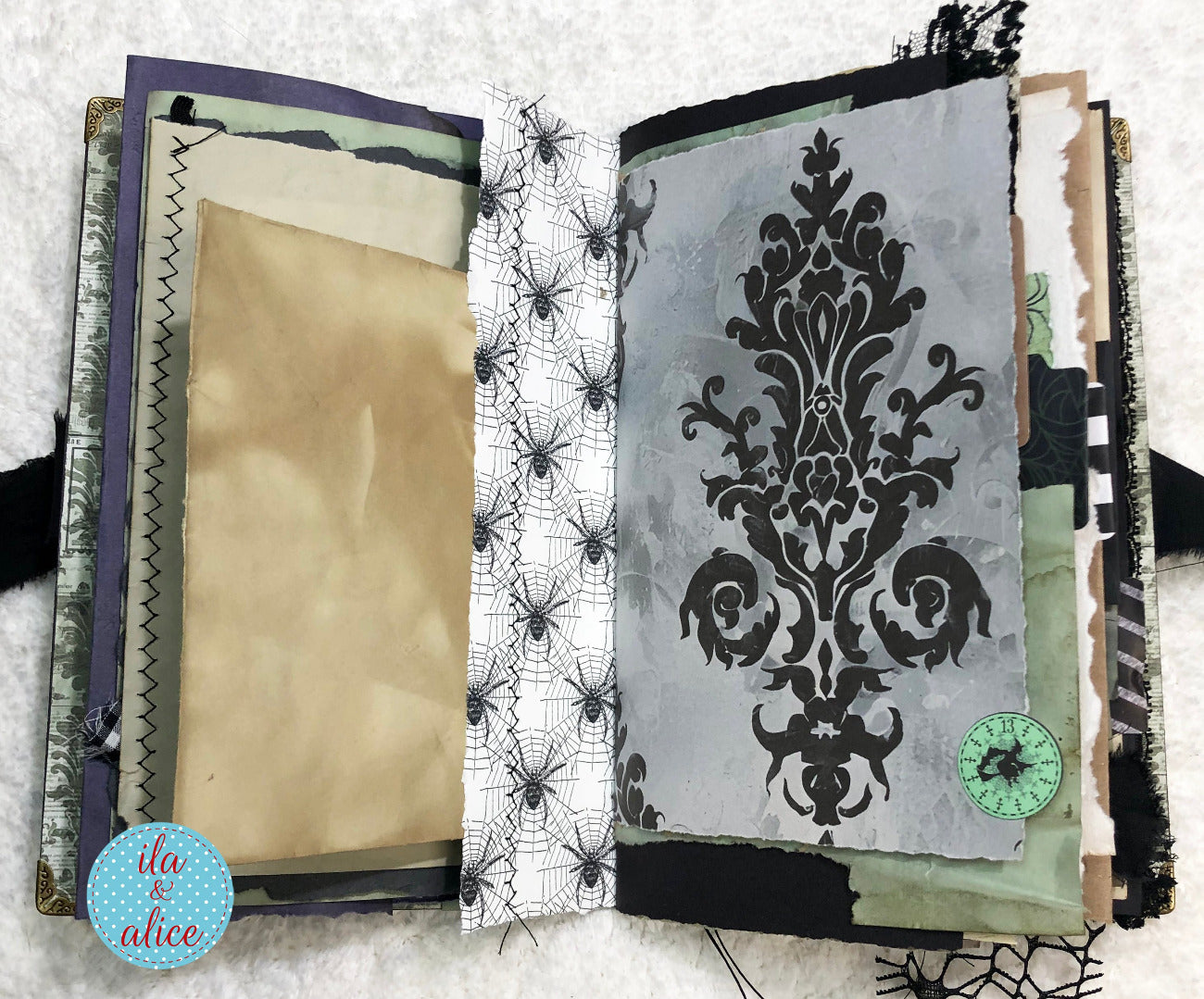 Handmade Eerie Halloween Gothic junk journal with decorative pages featuring spider webs and a damask pattern on a textured surface.