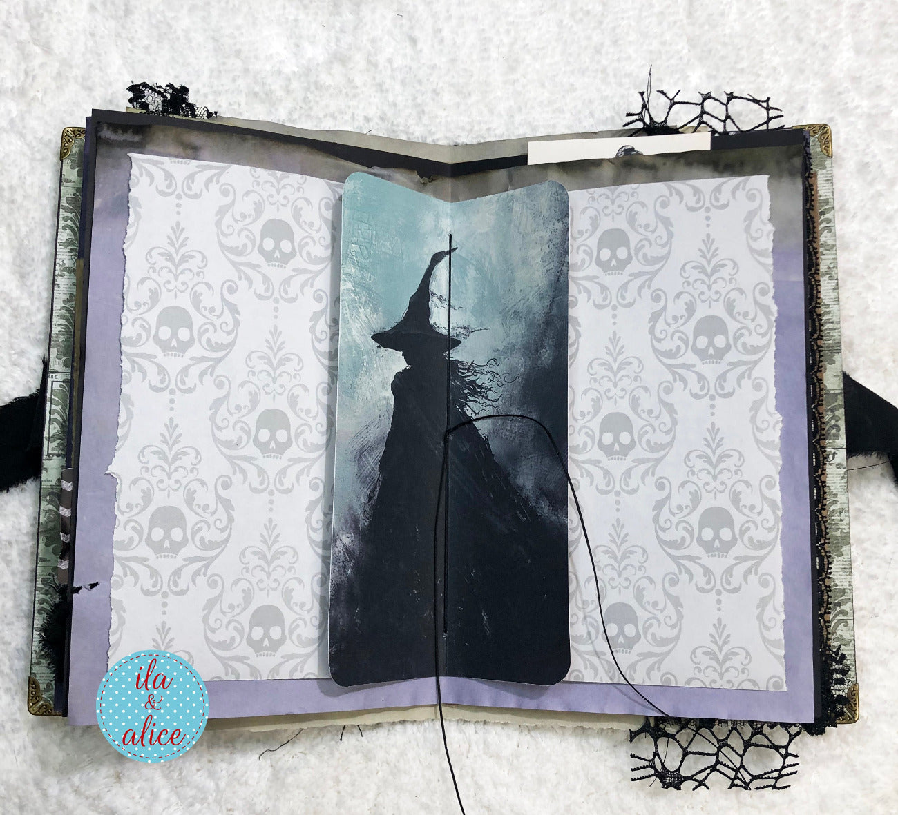 Handmade Eerie Halloween Gothic junk journal with a silhouette of a witch on a broomstick against a skull-patterned background, with 'ila alice' branding.