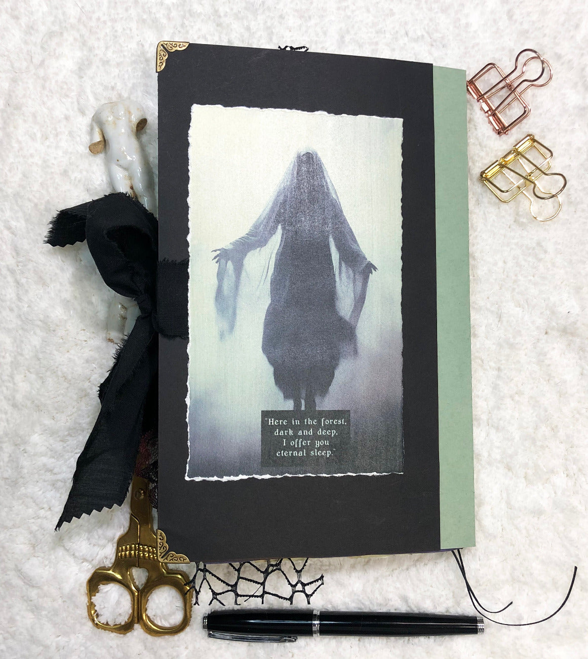 Black notebook with a ghostly illustration on a textured white surface with decorative items.