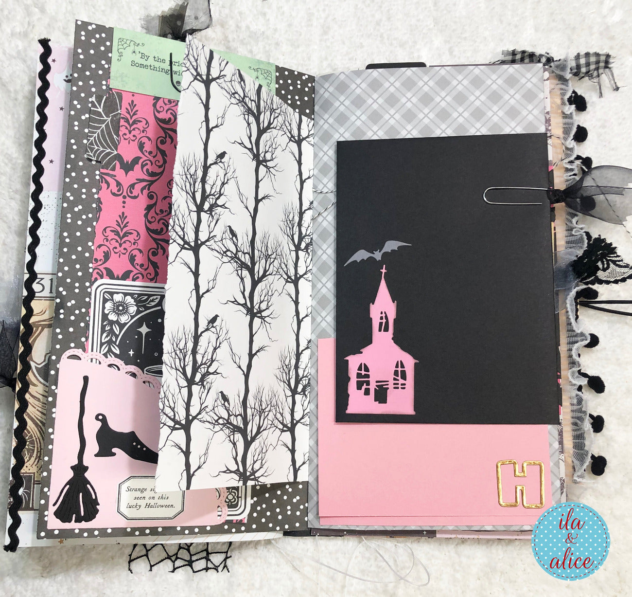Handmade Pink and Black Halloween junk journal with Halloween-themed pages featuring trees, a church, and brooms.