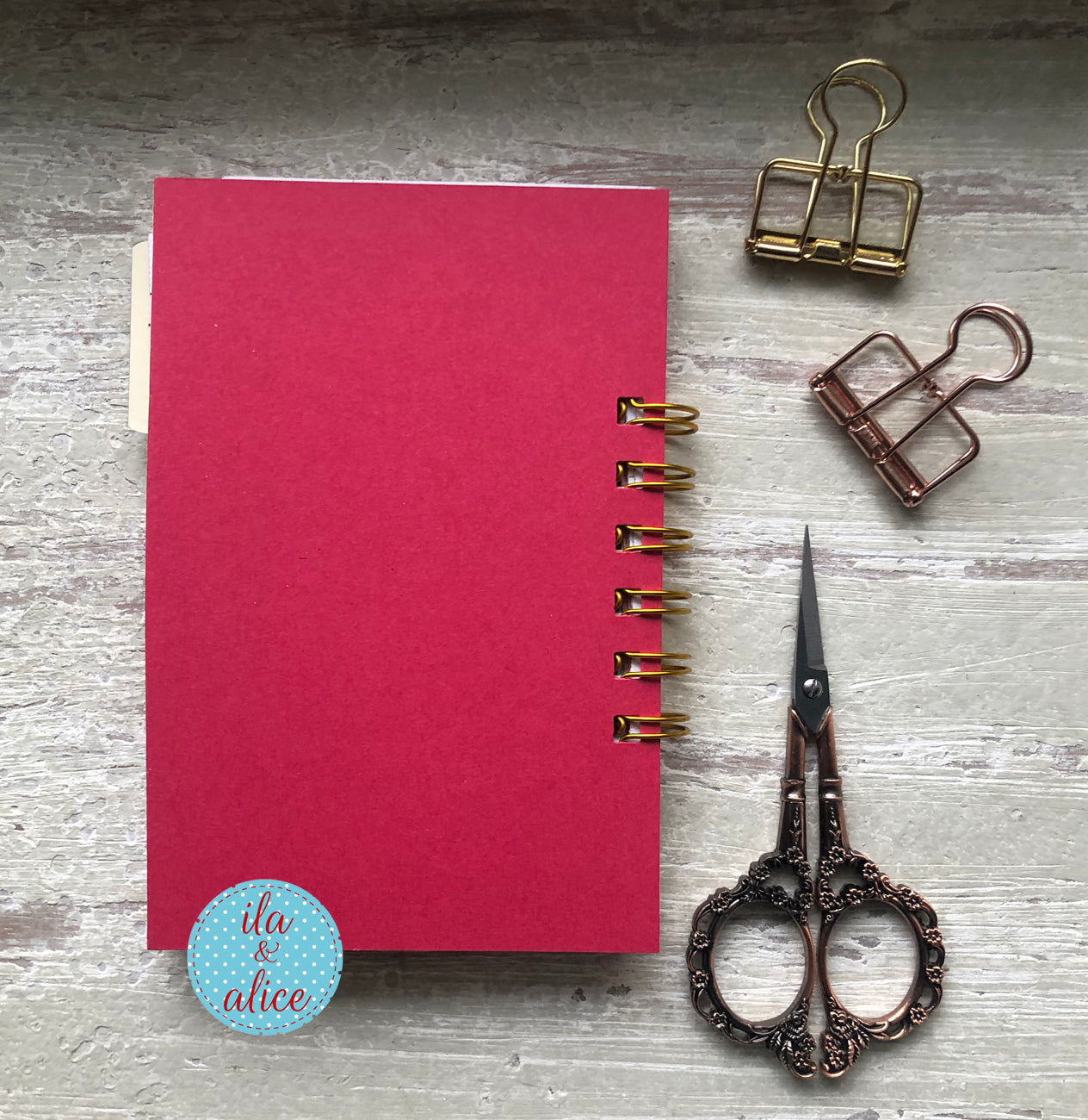 Red notebook with gold rings, vintage scissors, and paper clips on a gray surface.