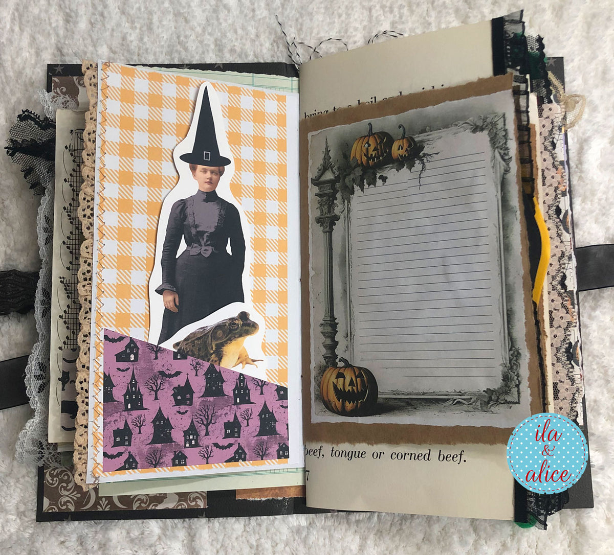 An open handmade scrapbook journal with Halloween-themed pages, featuring a witch cutout, a purple cat-patterned section, and a lined note card decorated with pumpkins. The journal is laid flat on a white textured fabric background.