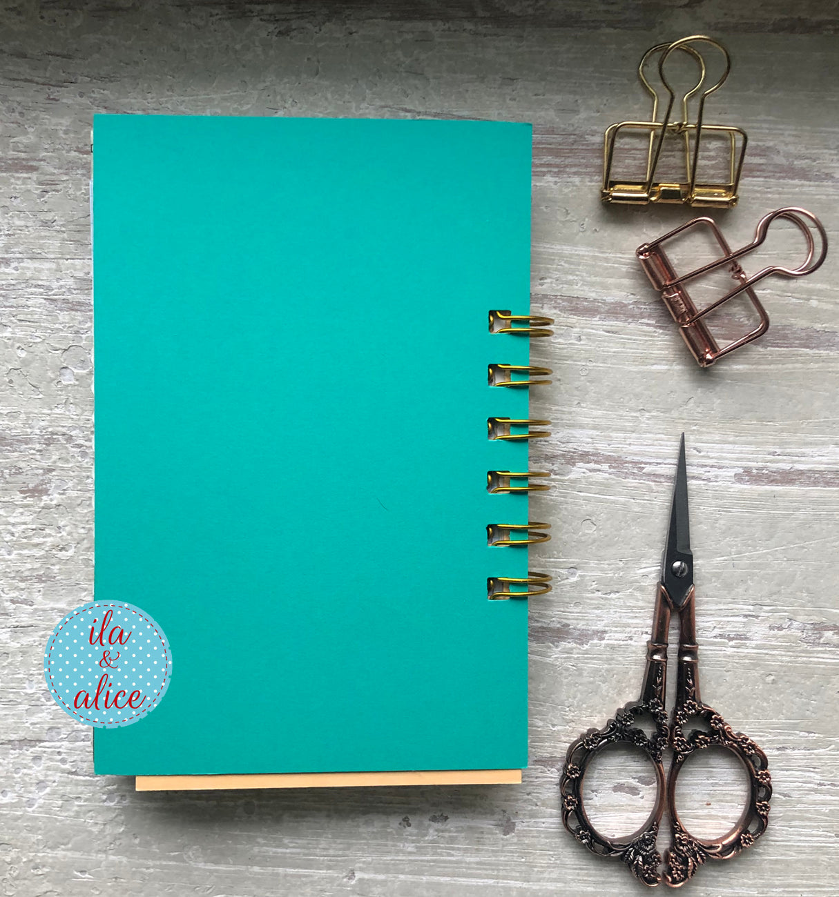 Teal notebook back with gold rings, vintage scissors, and paper clips on a gray surface.