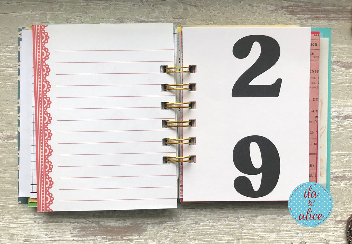 Open planner with lined pages and a page with the number 29 on a wooden surface, featuring the brand 'ila & alice'.