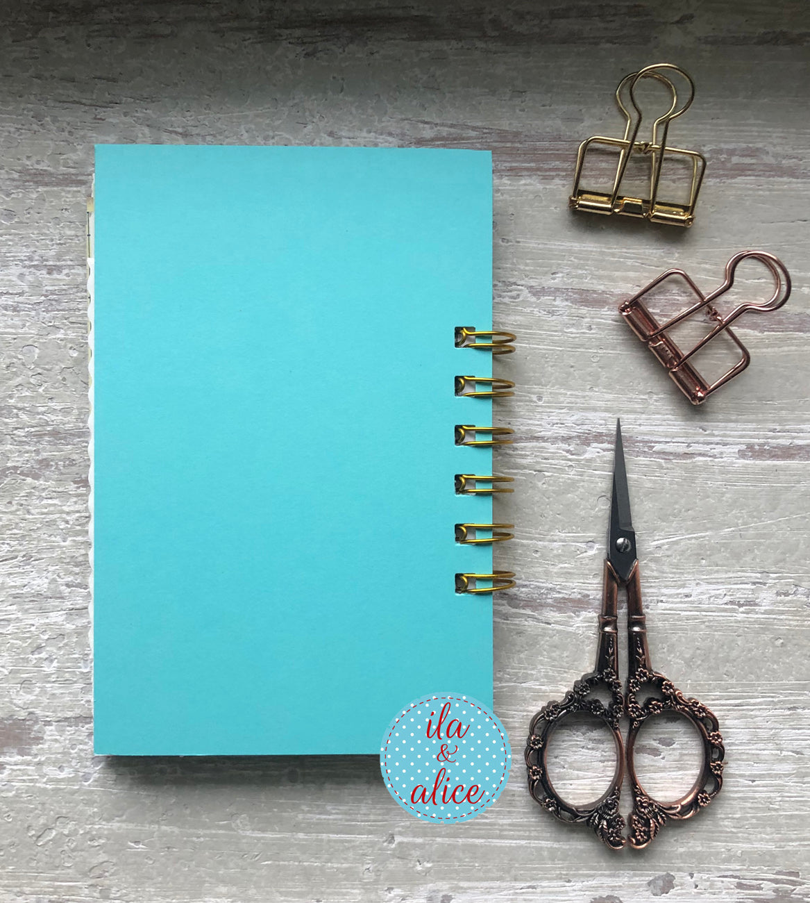 Blue notebook with gold rings, scissors, and paper clips on a wooden surface.