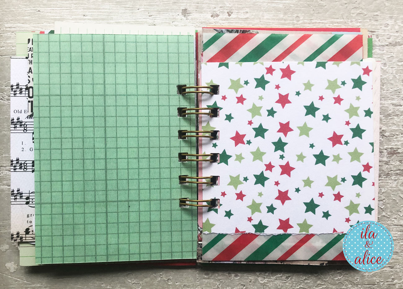 An open handmade spiral-bound planner or notebook showing decorated pages. The left page is light green grid paper, and the right page has a white background with red and green star patterns and striped paper borders.