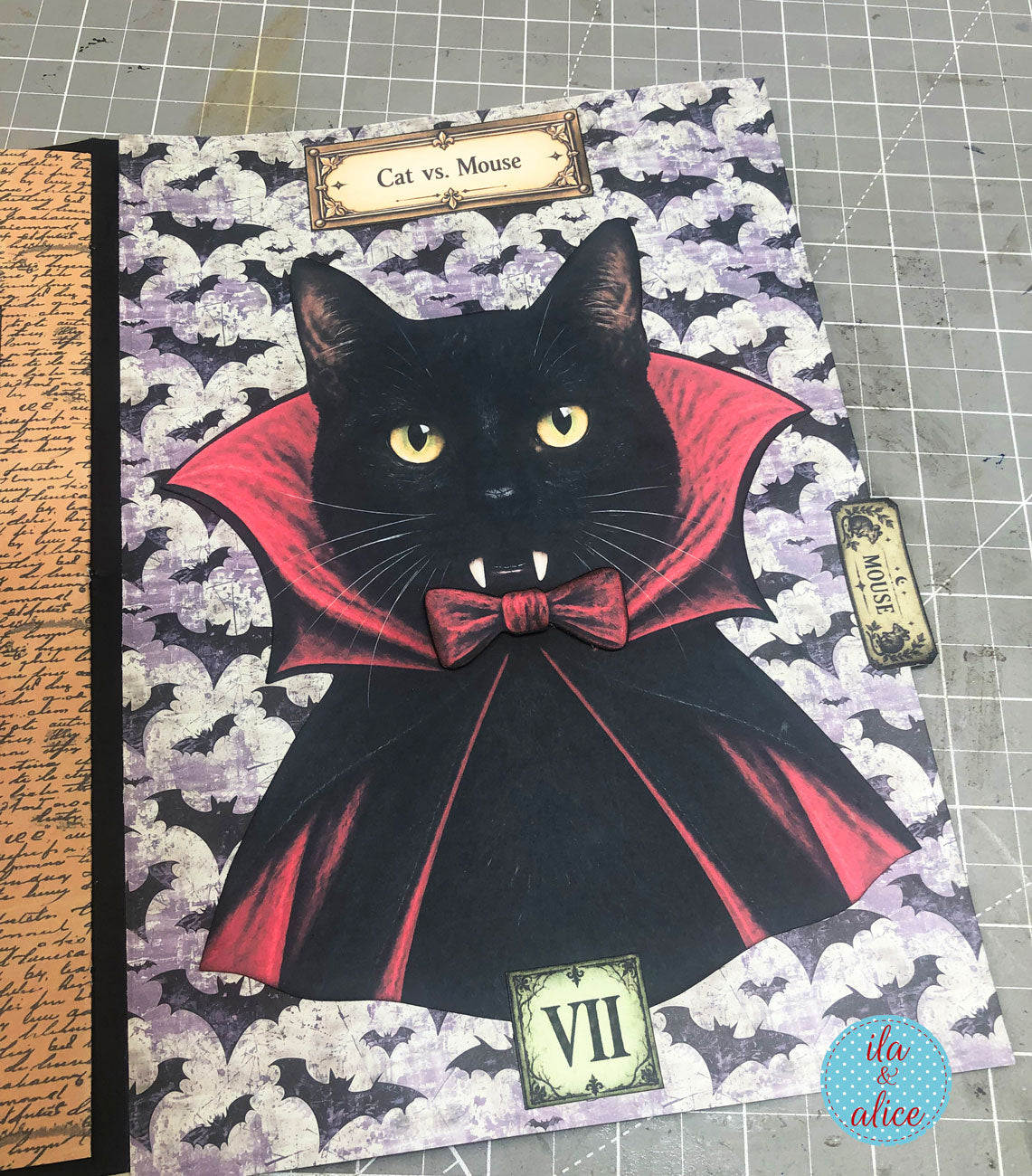 Interactive Halloween journal page featuring a black vampire cat in a red cape, a small mouse pull tab, bat-patterned paper, and a “Cat vs. Mouse” label.