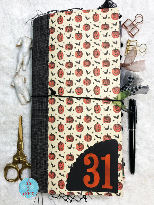 Handmade Halloween Junk Journal with Halloween design featuring pumpkins and the number 31, surrounded by stationery items on a textured surface.