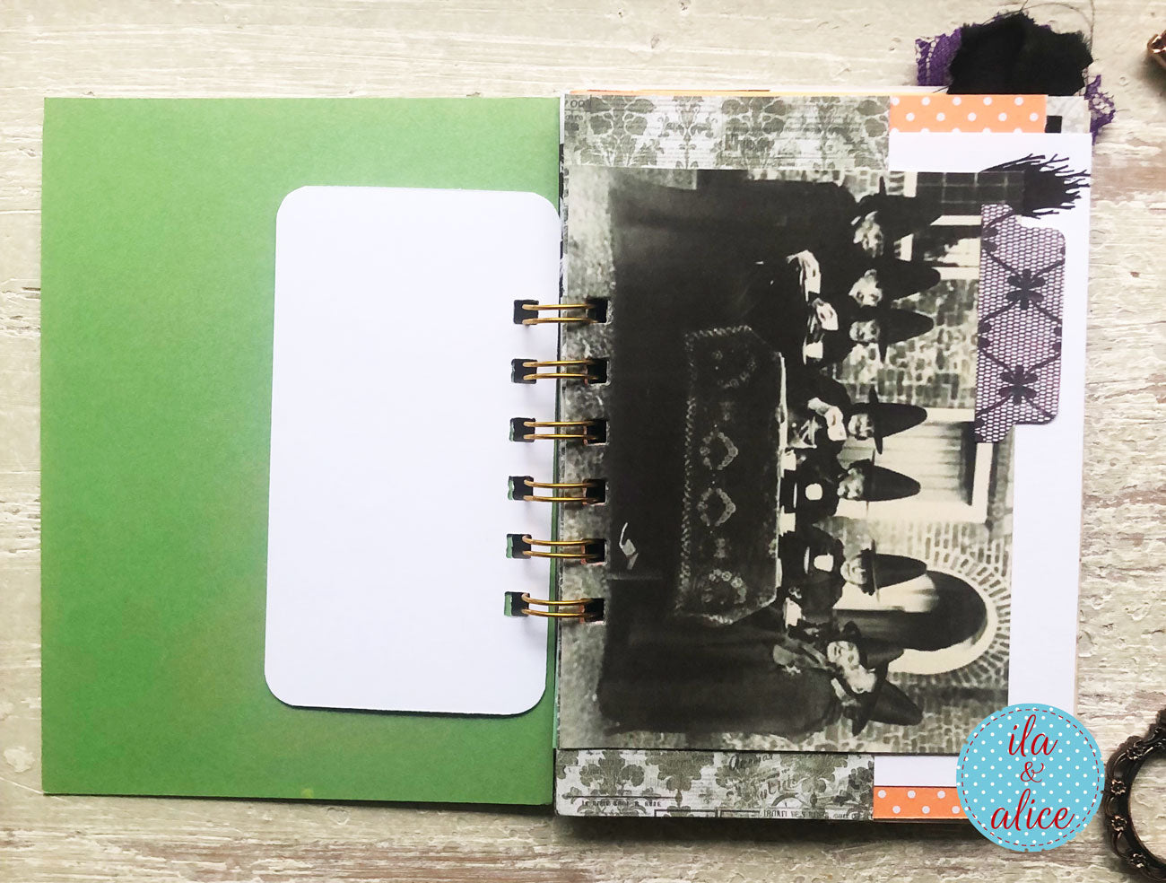 A handmade spiral-bound scrapbook journal or notebook shown open on a light wood surface. The left page is solid green with a blank white rectangular card attached.