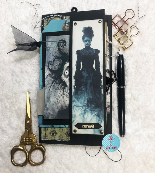 Halloween folio with a vintage-style female ghost and text 'cursed', accompanied by scissors and a pen on a textured surface.