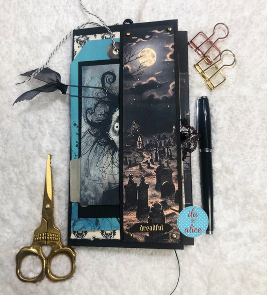 Decorative handmade Halloween creepy folio with Halloween-themed design, scissors, pen, and paper clips on a textured surface.