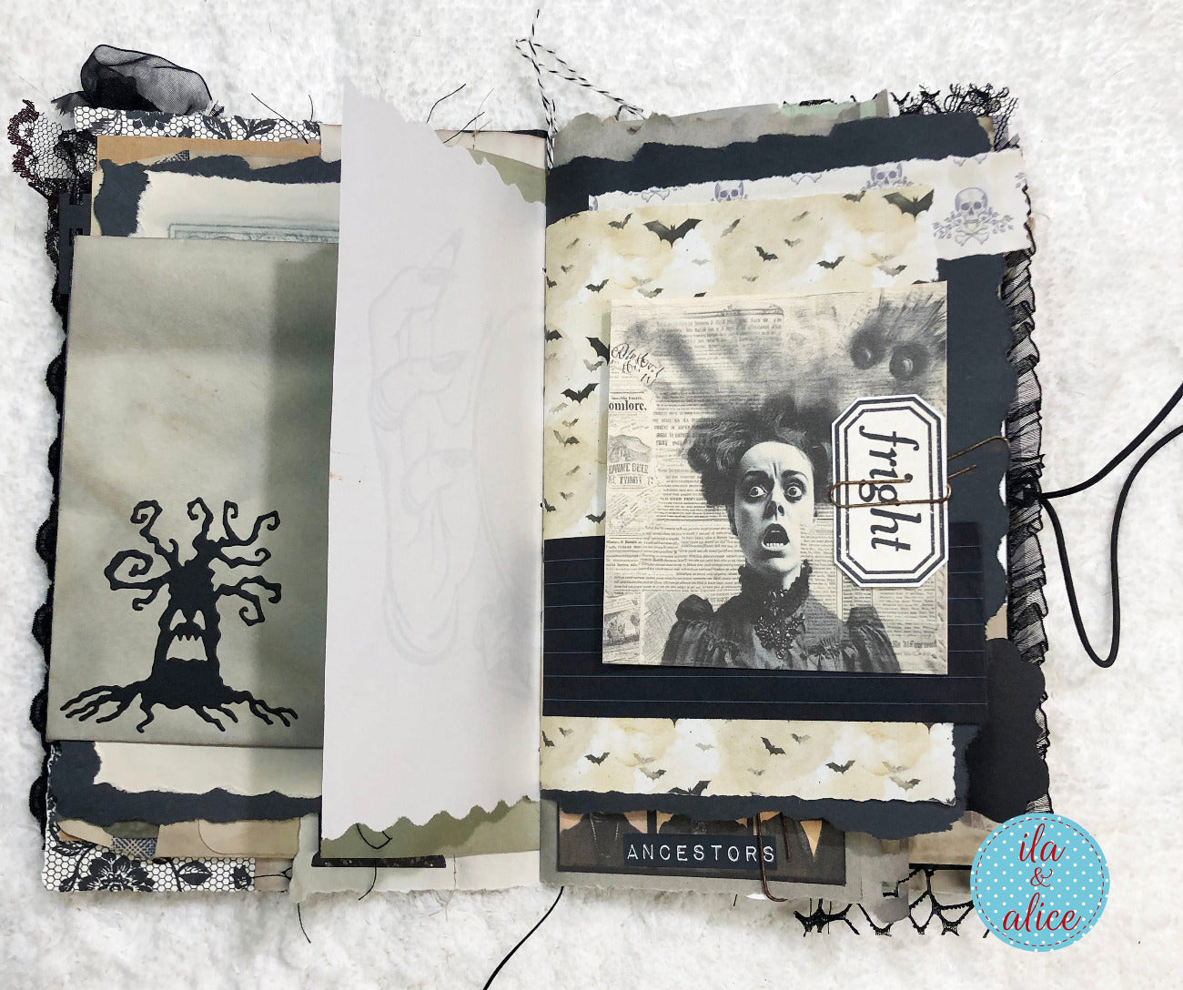 A handmade gothic-themed scrapbook album or journal shown open on a white textured fabric background. The pages feature vintage collage elements including newspaper clippings, black bat silhouettes, a ghost illustration, torn black ribbon, and a small 'finetti' brand tag.