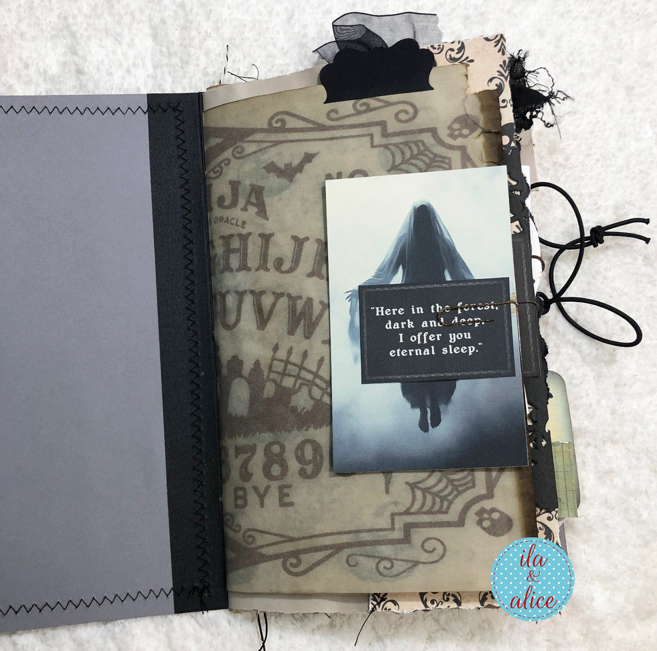 A handmade gothic-themed journal page featuring a black and white photo of a ghostly figure, a quote card reading 'Here in the forest, dark and deep, I offer you eternal sleep', a vintage-style ouija board background, black lace, ribbon, and a gray paper insert, all arranged on a white textured fabric background.