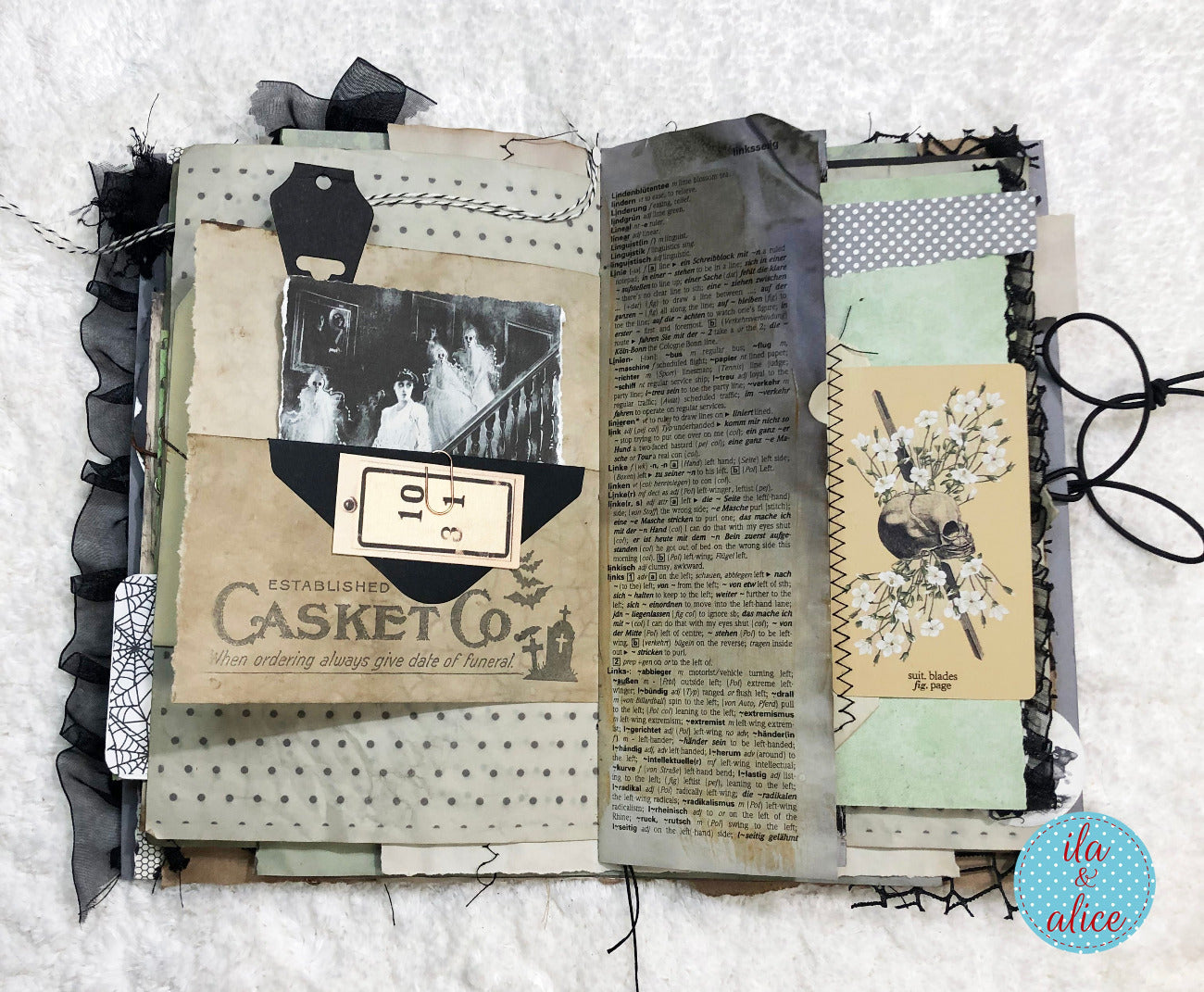 An open handmade scrapbook journal or art journal displayed on a white textured fabric background. The page features layered vintage-style elements including black ruffled trim, patterned paper, a black-and-white photo print, a piece of aged paper with text, a floral card, and a small bird illustration.