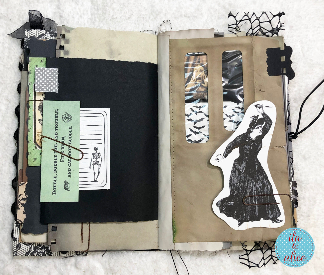 An open handmade gothic scrapbook journal or art journal spread on a white textured fabric background. The left page features layered paper elements including black cardstock, patterned tape, a light green card with a skeleton drawing and the text 'Double double double trouble Double double double trouble Double double double trouble', and a skeleton sticker.
