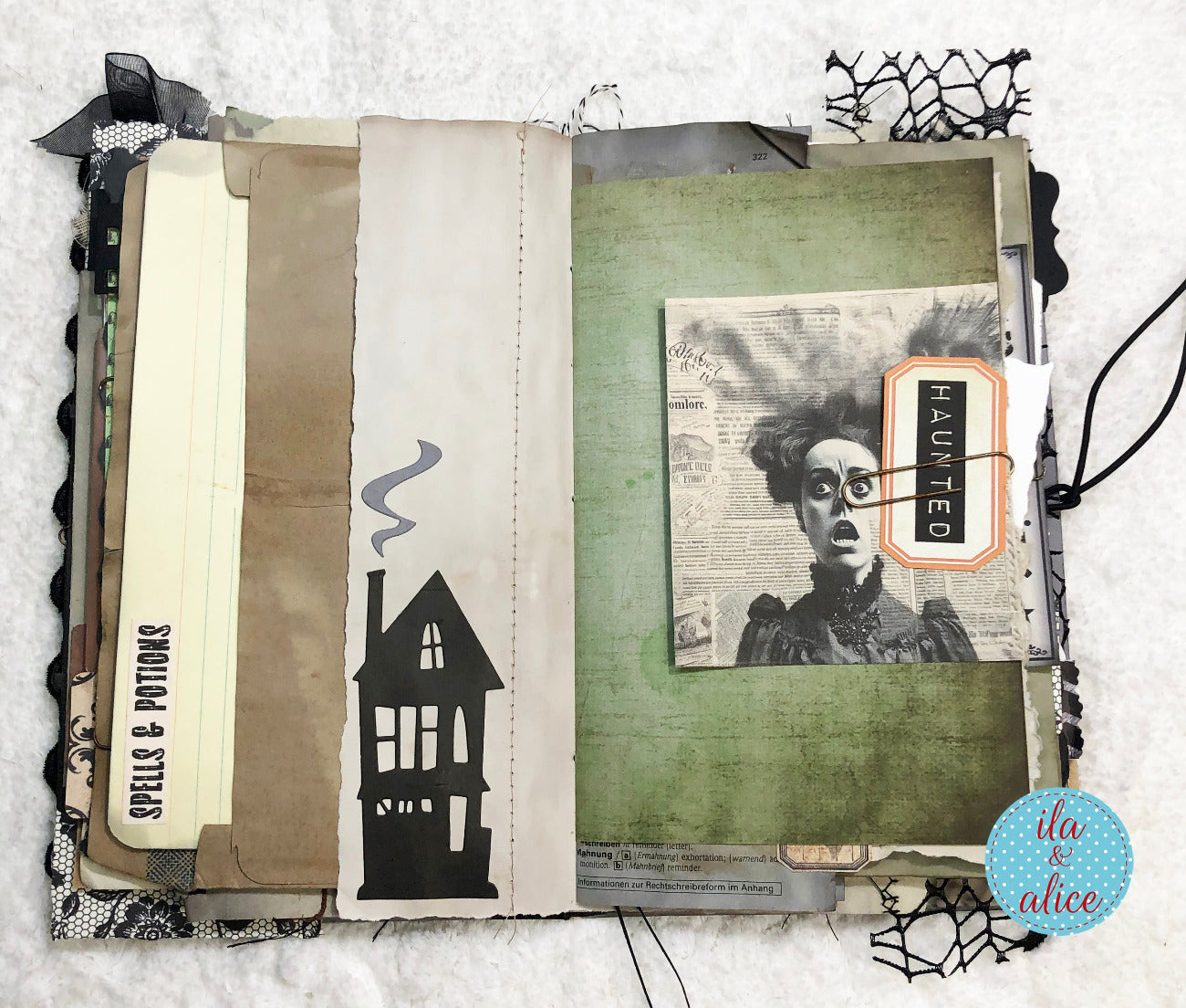 An open handmade scrapbook journal with a gothic Halloween theme, featuring layered paper tabs, a green textured background, a black house silhouette, a vintage-style portrait cutout, and a 'HAUNTED' tag on a white textured fabric background.