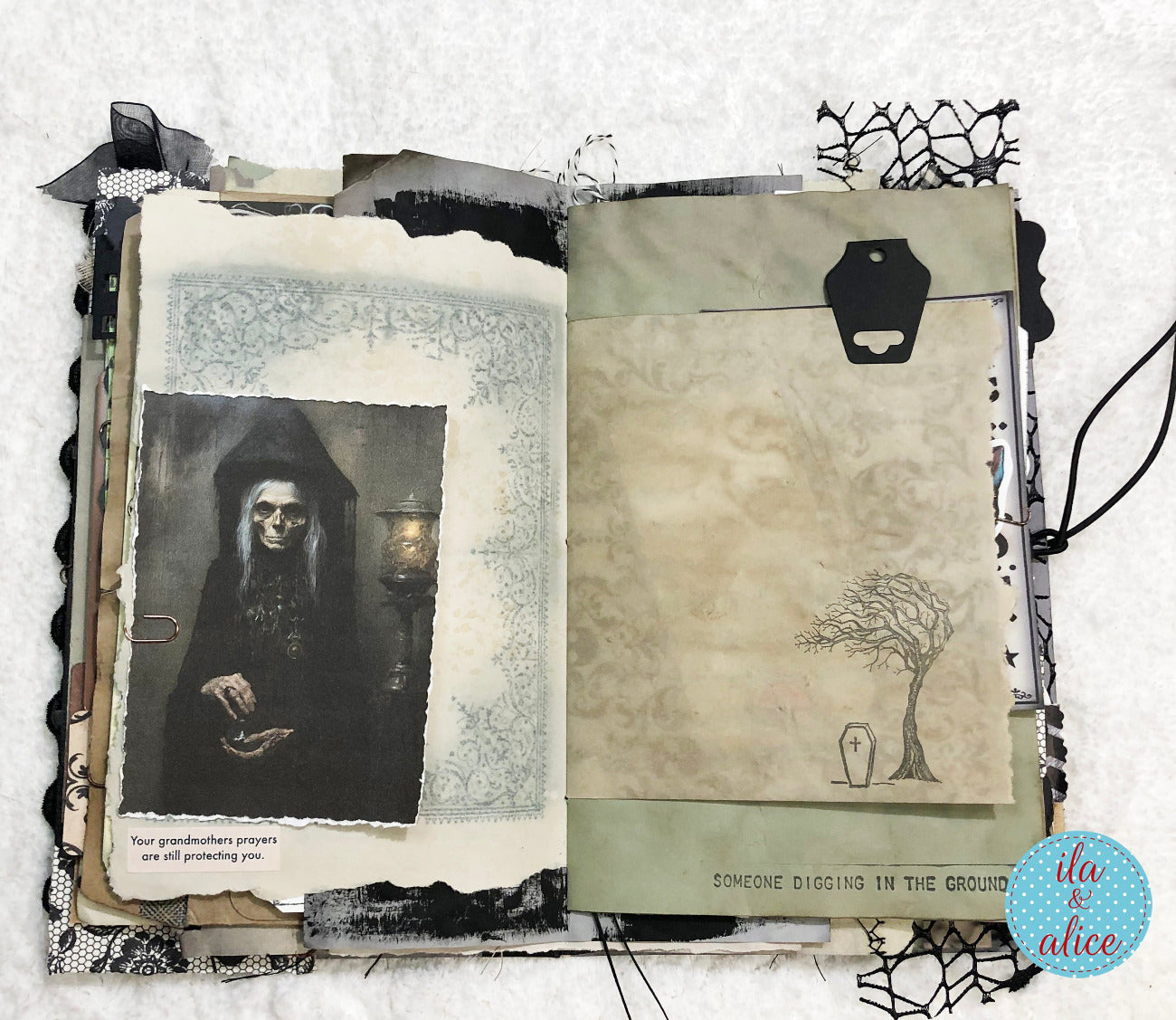 An open handmade scrapbook journal with distressed, vintage-style pages. The left page features a black-and-white photo of a hooded skeleton figure, while the right page has a beige textured panel with a simple tree and tombstone illustration, black tape, and decorative paper edges.