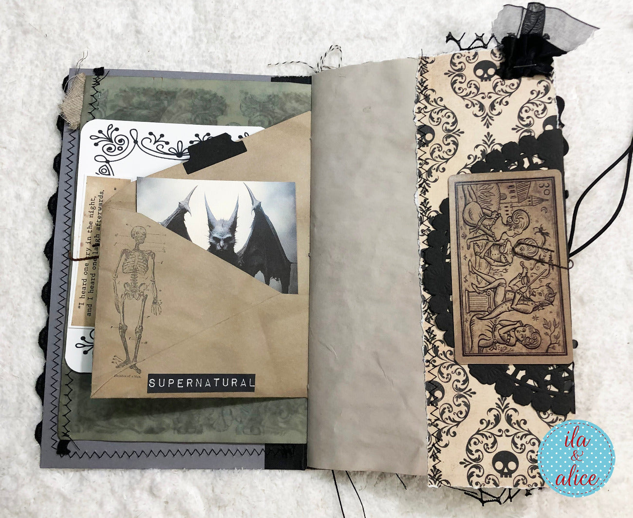 An open handmade scrapbook journal with gothic and horror-themed decorations, including a skeleton illustration, a bat photo, a 'SUPERNATURAL' label, skull-and-damask patterned paper, black lace, and a small black ribbon bow on a white textured background.
