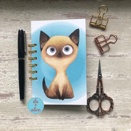 Mini junk journal with wide-eyed cat illustration on blue background, handmade vintage-style notebook with spiral binding