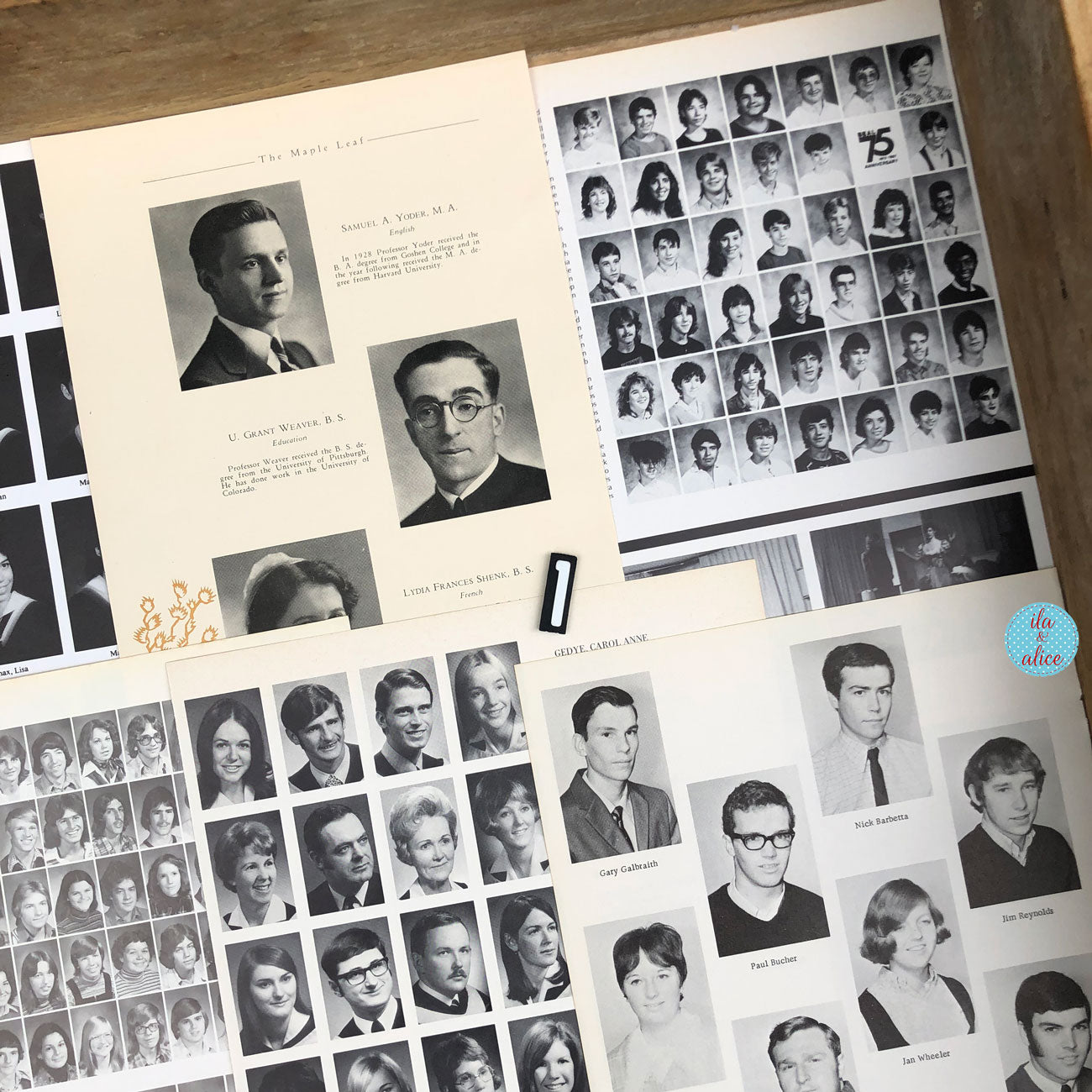 A close-up of a vintage or antique yearbook or alumni photo album spread out on a wooden surface. The pages contain multiple black-and-white portrait photographs of graduates, printed text, and grid layouts of student portraits.