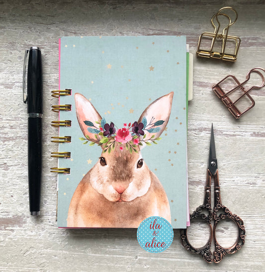 Notebook with rabbit illustration, pen, scissors, and clips on a wooden surface