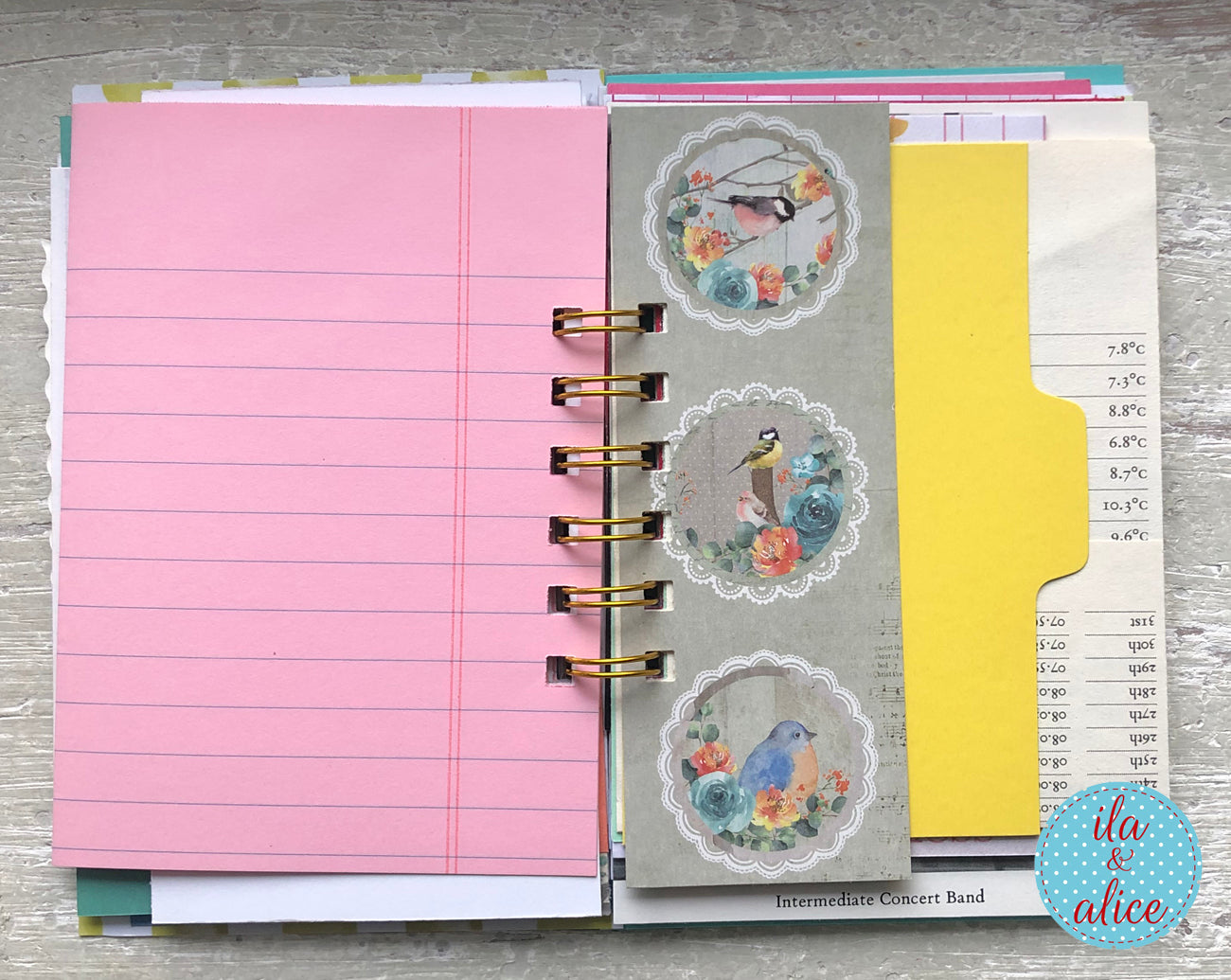 Planner with pink pages, floral stickers, and a yellow divider on a wooden surface.