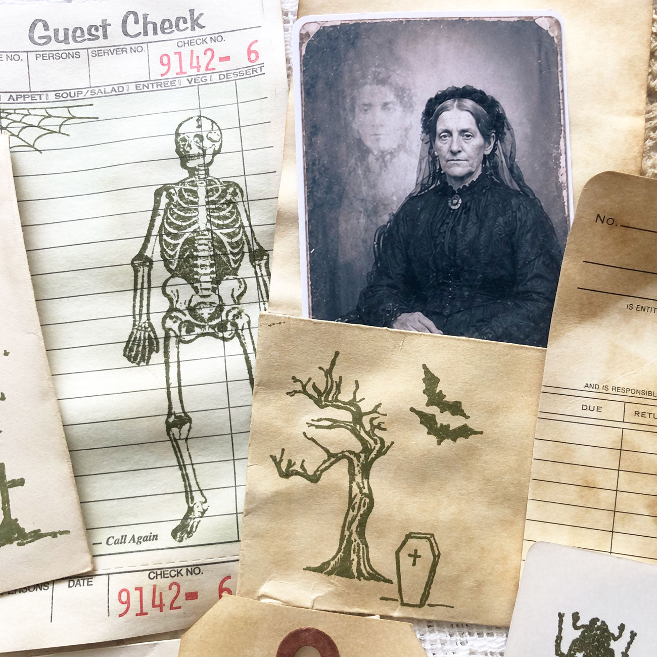 Close-up of gothic junk journal supplies including coffee-dyed tags, spooky stamps, and vintage-style portraits.