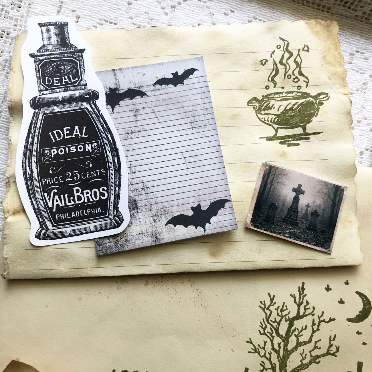 Close-up of gothic junk journal supplies including coffee-dyed tags, spooky stamps, and vintage-style portraits.