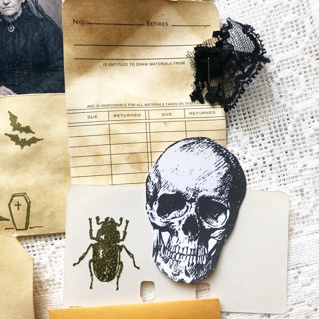 Close-up of gothic junk journal supplies including coffee-dyed tags, spooky stamps, and vintage-style portraits.