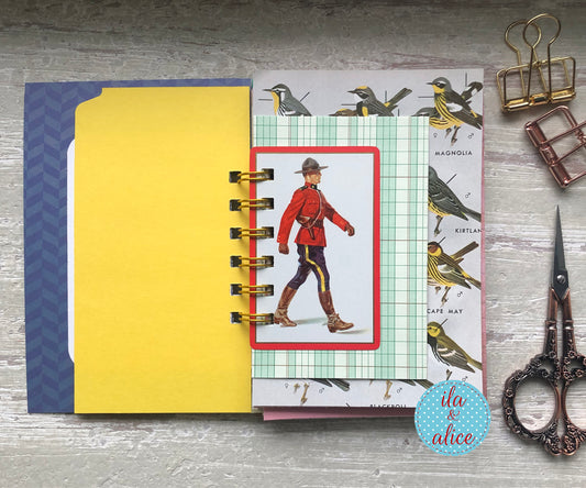 Notebook with bird illustrations and a character in a red uniform on a wooden surface with stationery items.