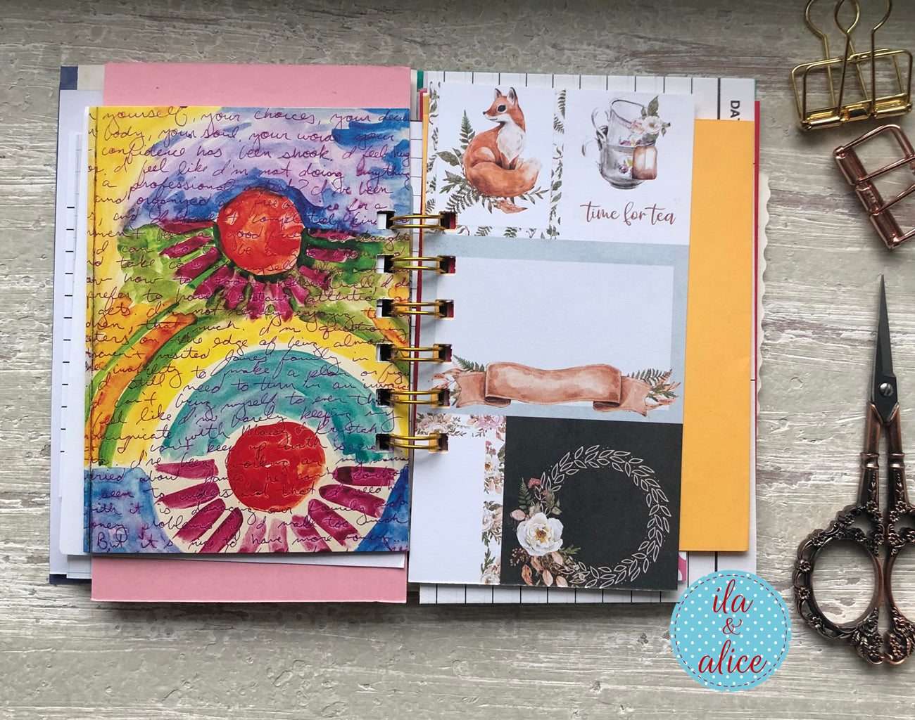 Open planner with colourful pages on a wooden surface, featuring a brand logo in the corner.
