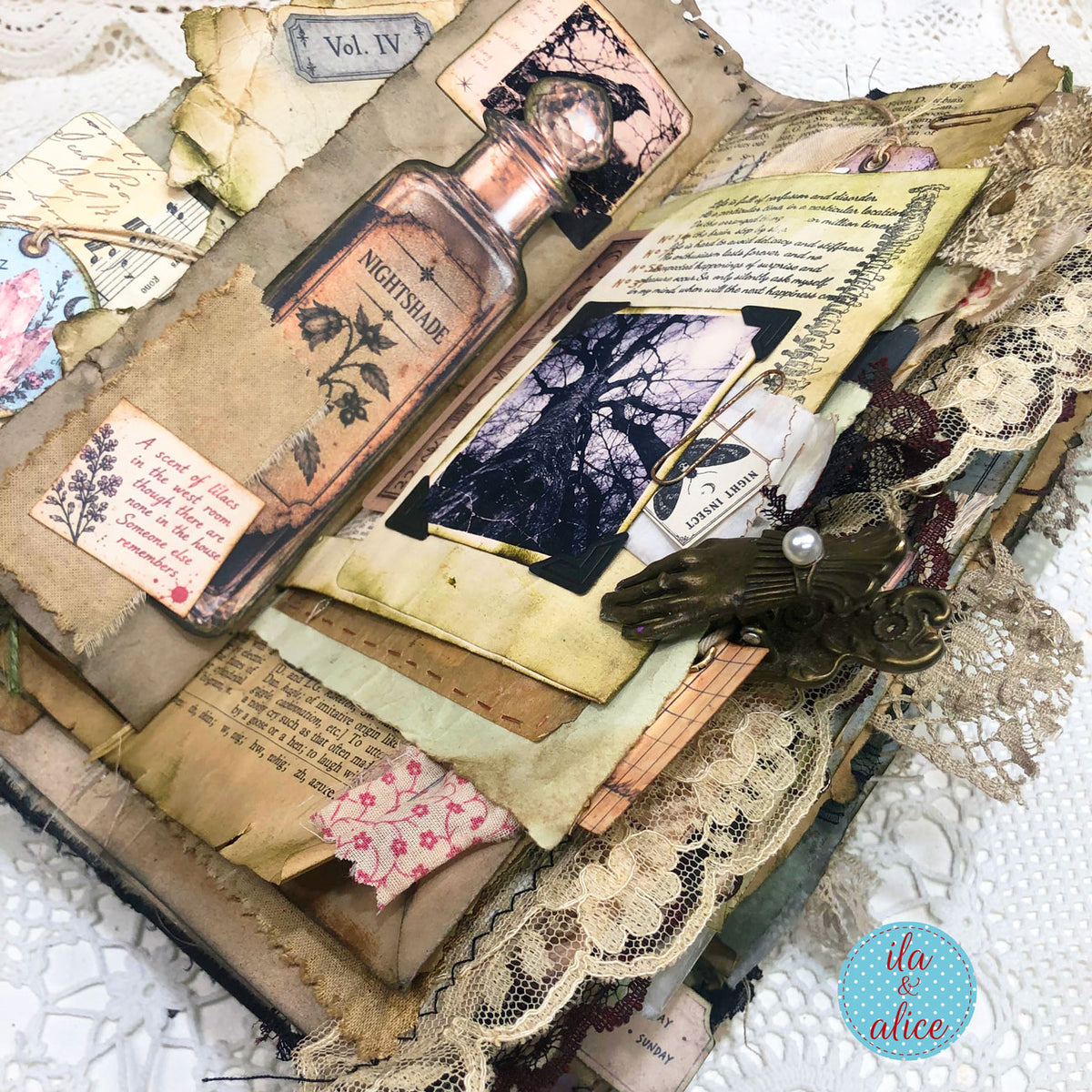 Close-up of the one-of-a-kind handmade witch’s grimoire with Nightshade bottle, eerie tree photograph, aged papers, antique lace and bronze hand clip.