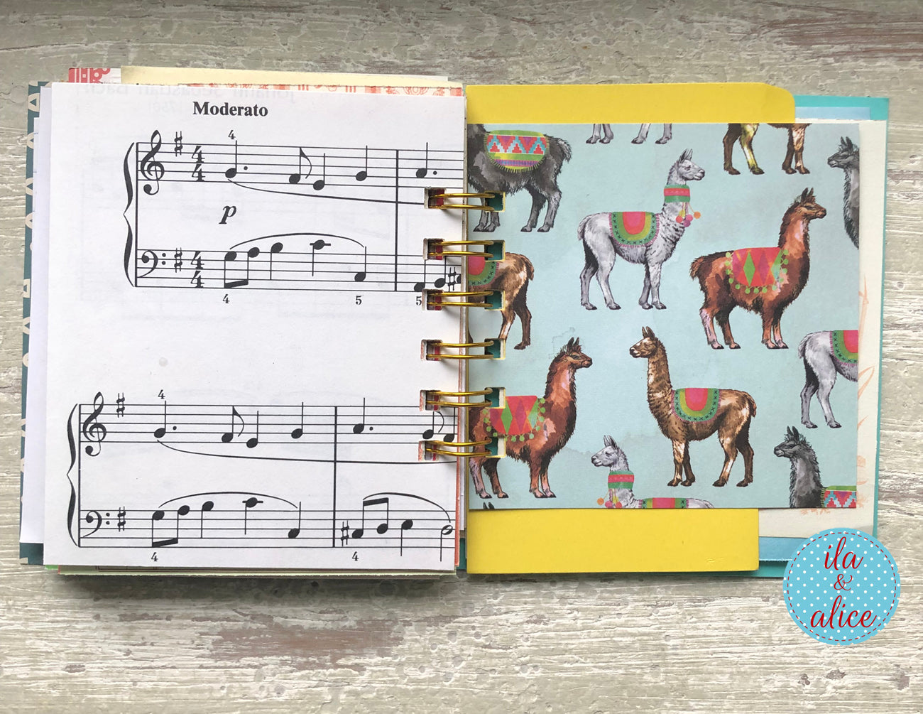 Notebook with music notation and a colorful page of llamas on a wooden surface.