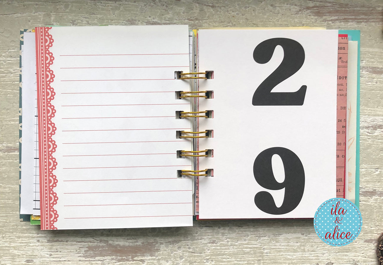 Open planner with lined pages and a page with the number 29 on a wooden surface, featuring the brand 'ila & alice'.