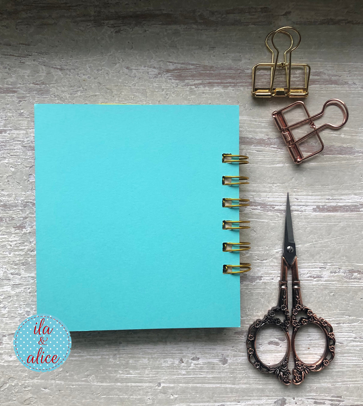 Blue notebook with gold rings, scissors, and paper clips on a gray surface