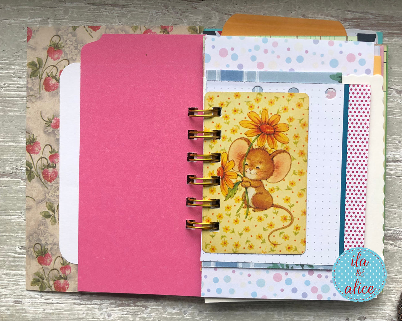 Open spiral-bound notebook with colorful pages and a decorative mouse illustration on a wooden surface.