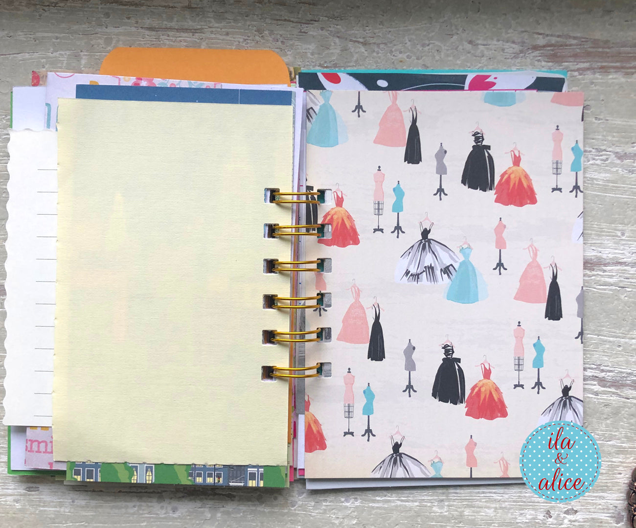 Open planner with colorful dress pattern on cover and plain page inside, on a wooden surface.